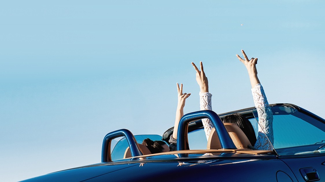 Zwei Frauen fahren in einem Cabrio weg und reißen die Hände in die Luft | Zulassungsservice
